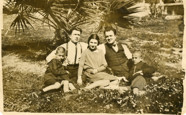 Photograph of two men, two boys and a girl sitting under a tree.