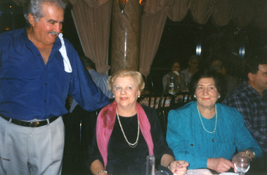 A man greeting two ladies who are seated at a table.