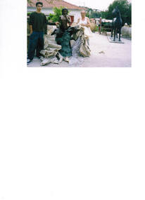 Two males unveiling a statue in a garden.