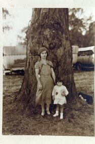 A young woman ands a little girl standing under a tree.