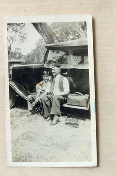 A man and a boy seated on the running board of a car.