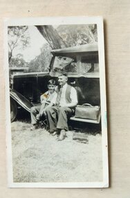 A man and a boy seated on the running board of a car.