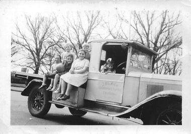 Five children are sitting on the back of a Chevrolet truck and another is in the cabin.