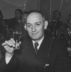 A head and shoulders photograph of a smartly dressed man preparing to toast someone at a function.