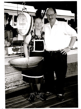 A man and a lady are standing beside their stall at the Victoria Market in MELBOURNE.