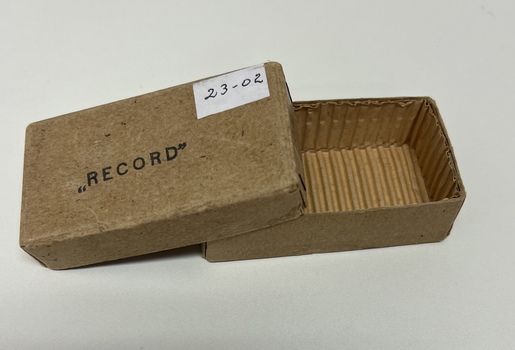 Small cardboard box used to hold a metal box containing glass syringes and metal needles. Cardboard box has RECORD stamped on the lid.