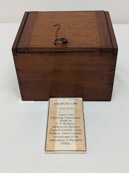 Photo shows the wooden box used to house the brass and glass microscope. Includes a written text regarding the past use of the  microscope.