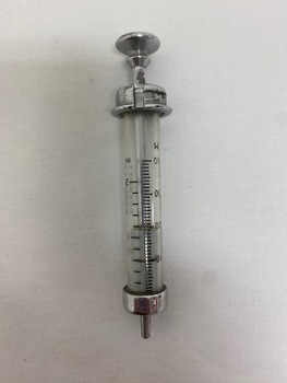 A glass syringe with graduation markings down the side, and a metal end for depressing the plunger and opposite end to attach needles.