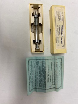 Glass Everett syringe with graduations marked on glass in a cardboard storage box with a Certificate of Examination document.