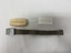 Degraded white plastic case with writing embossed on lid, fabric and metal tourniquet laid out flat