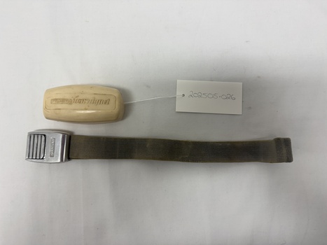 Degraded white plastic case with writing embossed on lid, fabric and metal tourniquet laid out flat