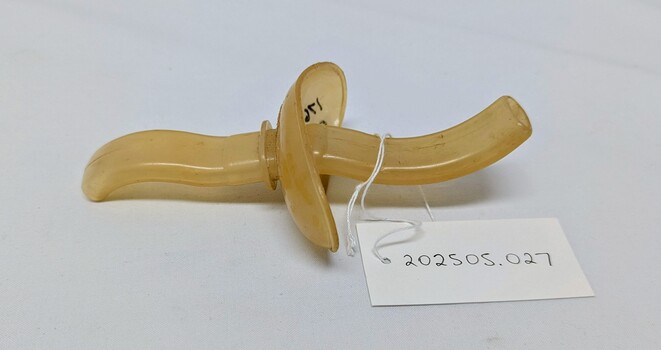 Johnson & Johnson Resusitube airway
An antique yellowed plastic object with curved handles and a central knob, labeled as item 202505.027.