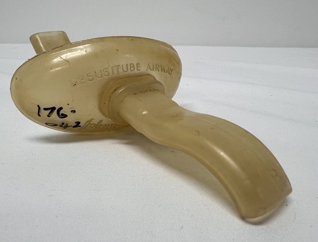 Vintage resuscitube airway device, yellowed plastic with markings, angled handle for emergency breathing assistance, shown on a white background.