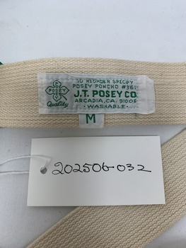 white label with green text on strapping - TO REORDER SPECIFY/POSEY PONCHO #3611/J.T.POSEY CO./ARCADIA, CA. 91006/.WASHABLE. LOGO OF 4 LEAF CLOVER TO THE LEFT OF LABEL, POSEY ACROSS VERTICAL AND HORIZONTAL LEAVES/Quality. underneath sizing label M