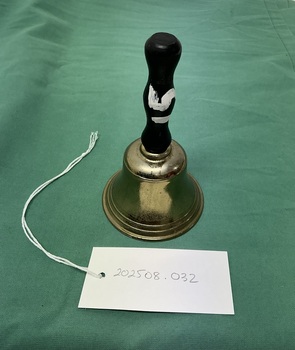 Small brass hand bell with a black wooden handle with a white painted number fifteen.
