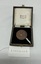 A medal with embossed design and Cyrillic text in a velvet-lined box, accompanied by a handwritten tag labeled "202509.008.