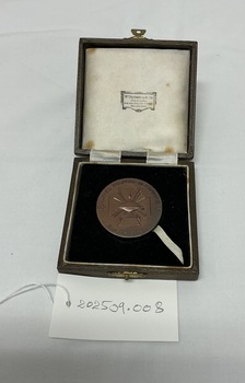 A medal with embossed design and Cyrillic text in a velvet-lined box, accompanied by a handwritten tag labeled "202509.008.