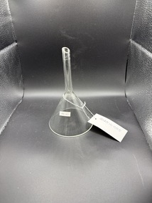 Clear glass funnel, sitting upside-down on its rim, the tip is cut at an angle.  The glass is 2mm thick and the edges raw but not sharp.