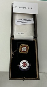  A display box with two badges: one with "AH" on a red cross, and another labeled "Hospital Nurses League." A tag above reads: “GORDON, LORNA J - 1943 AHNL BADGE, LOUISA MANN GOLD MEDAL.”.