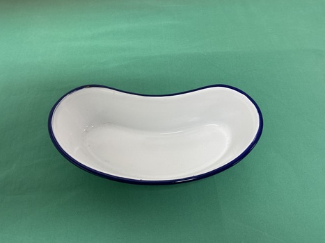 Small empty white kidney shaped ceramic dish with a dark blue rim viewed from above.