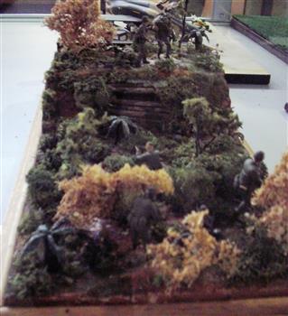 Handcrafted diorama of United States 29th Infantry in active battle with heavy artillery. One injured soldier being moved through jungle.