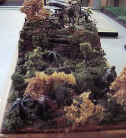 Handcrafted diorama of United States 29th Infantry in active battle with heavy artillery. One injured soldier being moved through jungle.