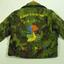 A child's bomber-style jacket made of khaki camouflage print polyester, hand embroidered and lined with blue.