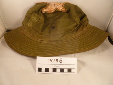 A Green giggle hat with a yellow-brown pig on top and an insignia with a crwon and star at the front