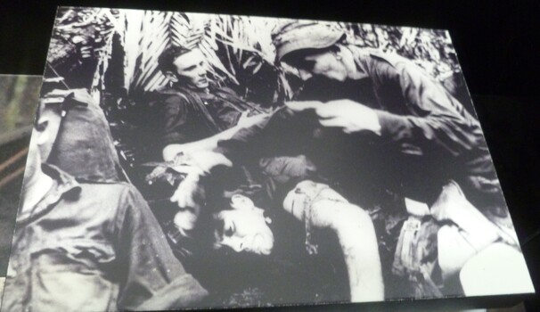 A black and white picture of a medic taking care of an injured soldier while the other two soldiers are waiting to be treated