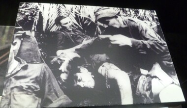 A black and white picture of a medic taking care of an injured soldier while the other two soldiers are waiting to be treated
