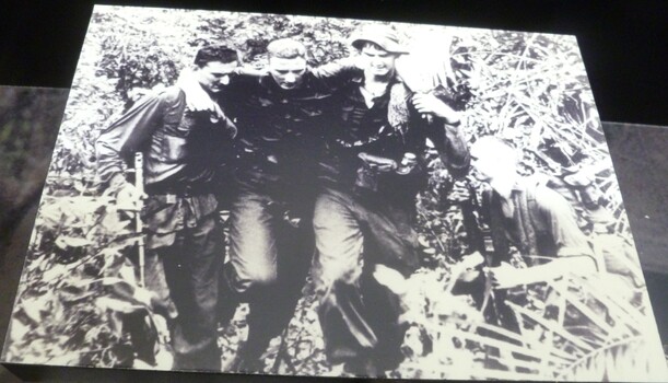A black and white photograph on black wood of four soldiers. 