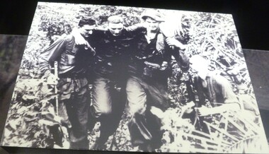 A black and white photograph on black wood of four soldiers. 