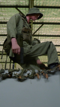 Australian tunnel rat in full combat uniform holding a pistol, crouched above a tunnel opening, shining a torch down the tunnel