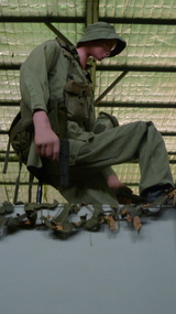 Australian tunnel rat in full combat uniform holding a pistol, crouched above a tunnel opening, shining a torch down the tunnel