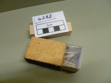 Functional Object, Box of matches to light burning fuses. Box is brown on top and bottom, sides have lightning strips. Box is displayed open with a clear cover to seal contents