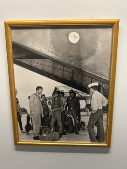 A Framed Black and White Photograph of People Gathered Under The Rear of a Caribou.