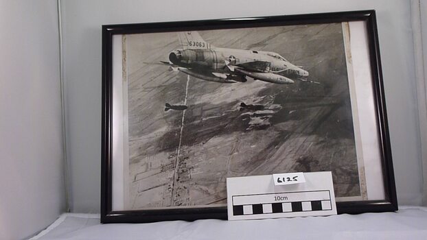 Black and white photograph in black frame depicting USAF Phantom 63063 dropping bombs.