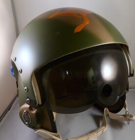 An Army green coloured flying helmet with goggles and webbed chin strap attached. An orange kangaroo logo painted on top of the helmet. 