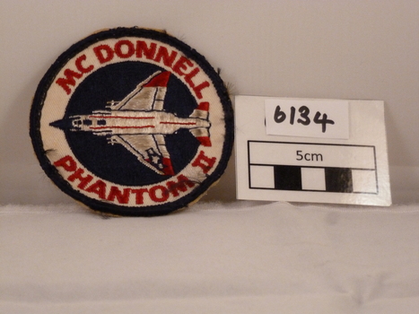 Circular woven cloth badge with Phantom air craft on it and red writing.