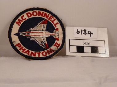Circular woven cloth badge with Phantom air craft on it and red writing.