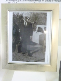 A picture of Errol W. Noack in light golden frame. He is wearing black suit and standing next to a white car. 