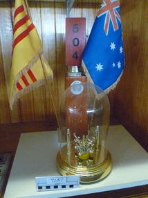 Flag, Wooden stand decorated with a Vietnamese flag and an Australian flag and the Vietnamese republic emblem, and a glass dome encasing a gold statuette display on a board base