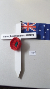 White Wooden Cross with red knitted poppy with green and black centre. The name Carver, Robert Charles 0119223 is stenciled on in black.