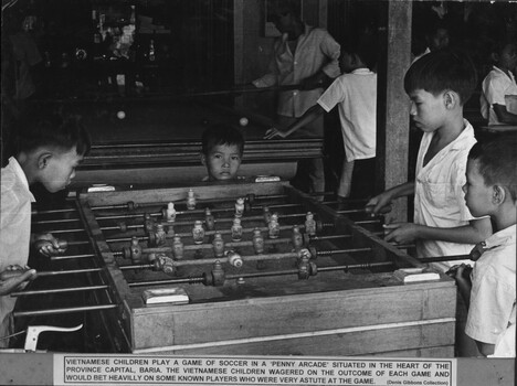 A black and white photograph of Vietnamese children playing a game of soccer in a Penny Arcade in the heart of the provincial capital Baria