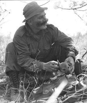 A black and white photograph of Sgt Bill O'Donnell and SGT Cook with D Company 6 RAR with a small puppy which became their mascot.