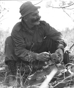 A black and white photograph of Sgt Bill O'Donnell and SGT Cook with D Company 6 RAR with a small puppy which became their mascot.