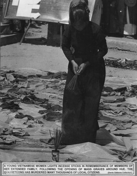 A photograph of a young Vietnamese woman lighting incense in remembrance of members of her extended family following the opening of mass graves around Hue