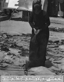 A photograph of a young Vietnamese woman lighting incense in remembrance of members of her extended family following the opening of mass graves around Hue