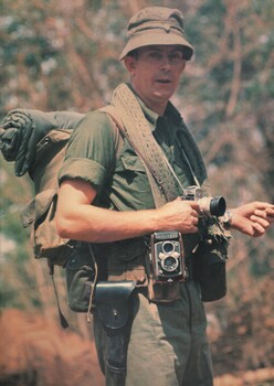 A photo of War correspondent Denis Gibbons in full pack waits to load into a Huey troop helicopter to commence a heli-borne assault.