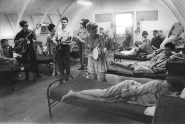 A photograph of Lorrae Desmond playing a tamborine and singing for sick and woulded American G.I's at the 135th Evac Hospital Bien Hoa. 